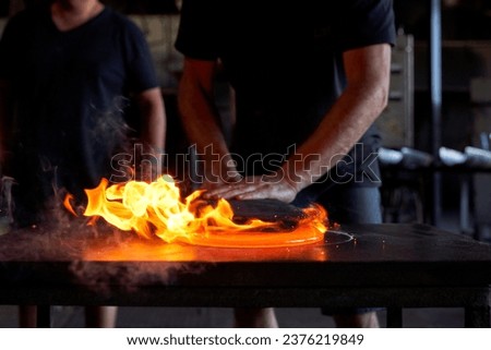 Faceless male glassmiths standing at workbench and forming burning liquid glass together in dark glassblowing workshop Royalty-Free Stock Photo #2376219849