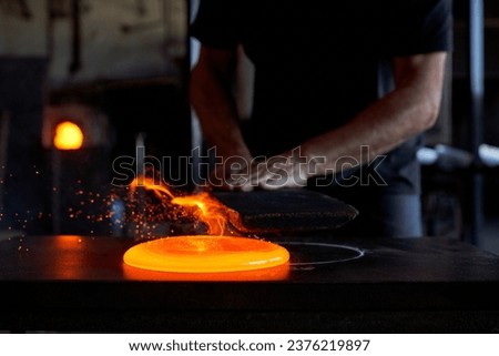 Unrecognizable male glassmith standing at metal workbench and working with hot liquid glass in darkness at glassblowing factory Royalty-Free Stock Photo #2376219897