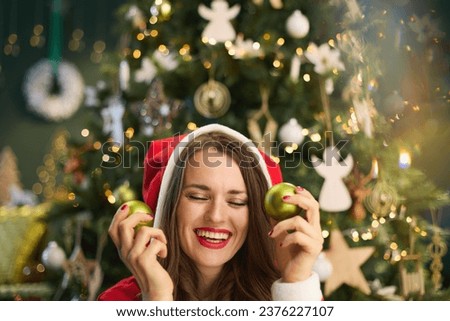Christmas time. smiling modern housewife with Santa hat and Christmas ball near Christmas tree in the modern house. Royalty-Free Stock Photo #2376227107