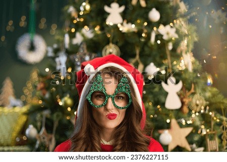 Christmas time. modern woman with Santa hat and funny Christmas tree glasses near Christmas tree in the modern house. Royalty-Free Stock Photo #2376227115