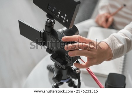 Unrecognizable blogger shooting video for online broadcast using professional equipment and taking notes in modern light room at home