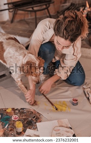 Creative female artist bonding with pet using paintbrush and paw print while drawing on fabric in modern studio