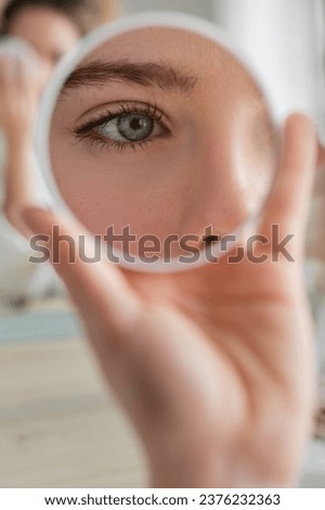 Eye of crop unrecognizable female reflecting in small round mirror in hand while sitting at table during daily routine at home Royalty-Free Stock Photo #2376232363