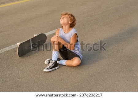 High angle of preteen boy embracing injured knee and suffering from pain after falling off skateboard Royalty-Free Stock Photo #2376236217