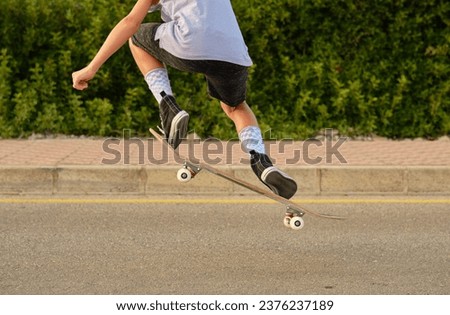 Back view of crop unrecognizable preteen skater in moment of jumping with skateboard over road in sunset