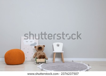 Kindergarten interior. Small chair, toy, ottoman and picture near grey wall, space for text