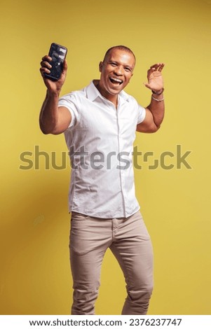 Portrait of a Brazilian wearing a button-up shirt and jeans, smiling and looking at the camera, holding his cell phone and showing it to the front - Belém - Pará - Brazil