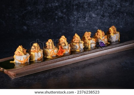 Appetizing sushi topped with salmon and fresh sauce served on wooden plate on marble table in restaurant against black background