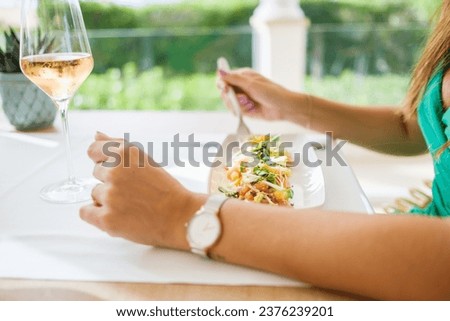 Side view of unrecognizable female sitting at table with plate of appetizing salad made of vegetables and shrimps garnished with grated cheese while having lunch in patio of restaurant in summer