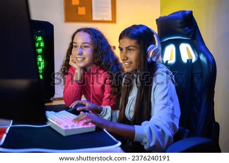 Positive teenage multiracial looking at screen of monitor while sitting at table with gaming pc and using keyboard to play game in room