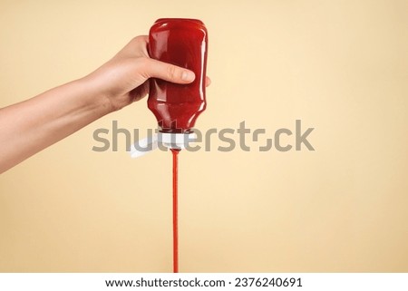 Woman pouring tasty ketchup from bottle on beige background, closeup. Space for text Royalty-Free Stock Photo #2376240691