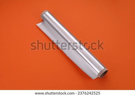 Roll of aluminum foil on orange background, above view