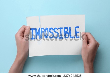 Motivation concept. Woman making word Possible from Impossible by tearing paper on light blue background, top view Royalty-Free Stock Photo #2376242535
