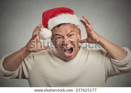 Closeup portrait headshot christmas man with red santa claus hat hands on head, stressed out, yelling, showing frustration. Negative human emotions face expression isolated on grey wall background