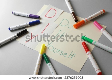 Sheet with written phrase Do It Yourself and colorful markers on grey background. DIY concept