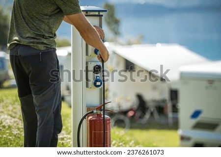 Motorhome RV Owner Attaching Power Cable to Camping Electric Post During Camping Stay Royalty-Free Stock Photo #2376261073