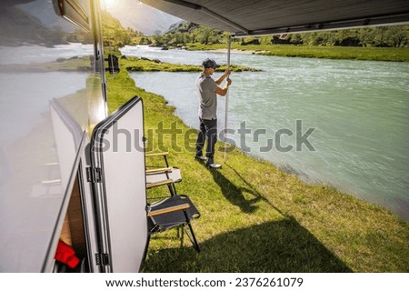 Caucasian Tourist and RV Owner Extending Awning While Camping Near Scenic Norwegian River Royalty-Free Stock Photo #2376261079