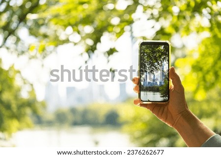 A person takes a mobile photo of the New York City's skyline seen through the trees of Central Park in New York, USA.