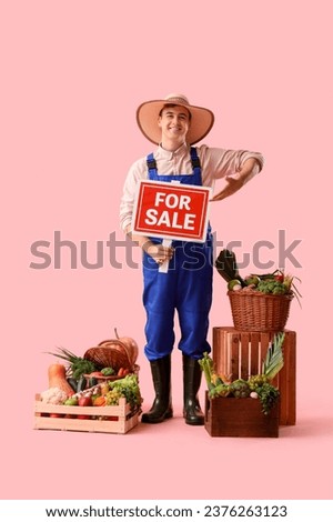 Male farmer with fresh vegetables and FOR SALE sign on pink background