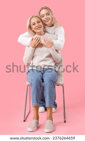 Happy young beautiful woman with her mother sitting on chair against pink background