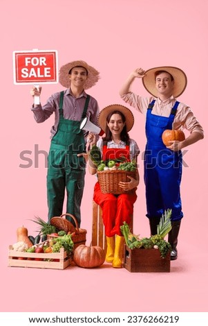 Young farmers with fresh vegetables and FOR SALE sign on pink background