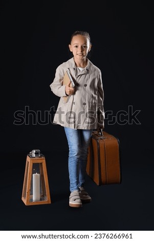 Cute little traveler with adventure book and suitcase on dark background