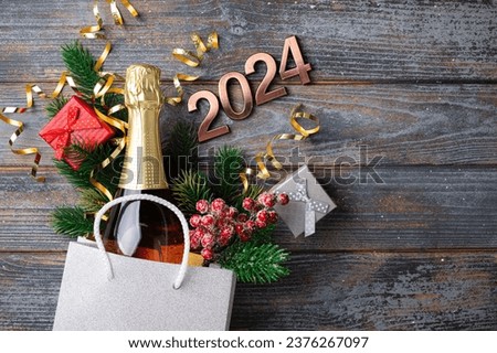 2024 New Year composition. New year holidays card with shopping bag with bottle of сhampagne, festive decorations. Gifts, present, festive New Year 2024 background. Copy space
