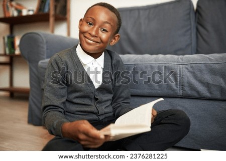 Cute brilliant smart child of african american ethnicity study at home, doing homework, sitting on floor with book in hands smiling at camera with enthusiasm, happy to get new knowledge Royalty-Free Stock Photo #2376281225