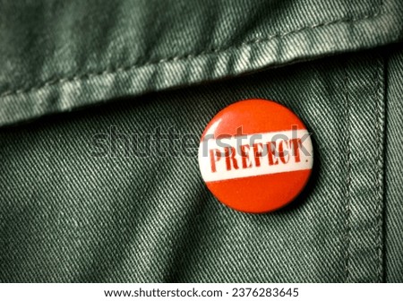 Vintage round school prefect tin pin button badge on green jacket taken in the United Kingdom October 2023 Royalty-Free Stock Photo #2376283645