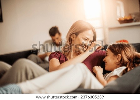 Happy young mother playing with her daughter on the couch at home Royalty-Free Stock Photo #2376305239