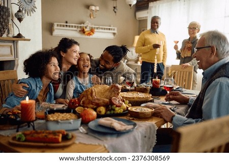 Happy multiracial parents and their kids laughing during family meal on Thanksgiving in dining room. 