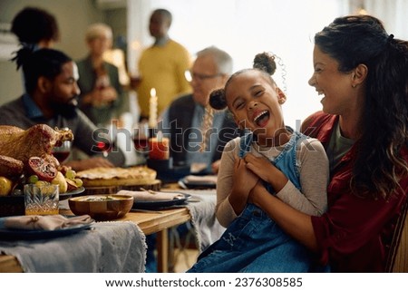 Happy African American girl and her mother laughing while gathering with their extended family on Thanksgiving at home. Royalty-Free Stock Photo #2376308585