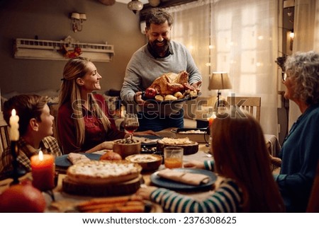 Happy father serving Thanksgiving turkey to his multigeneration family at dining table. Royalty-Free Stock Photo #2376308625