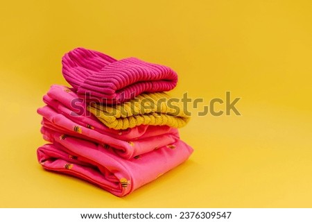 Stack of children's warm clothes and hat on yellow background. Kids pink clothes for spring, autumn or winter. Fashion kids outfit. 
