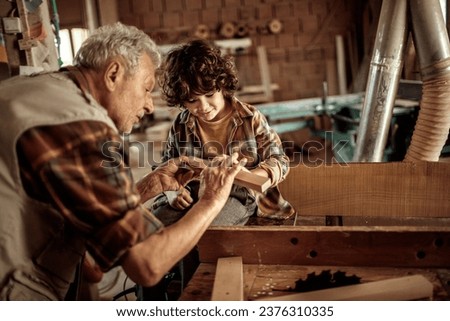 Young boy learning how to measure wood from his grandfather carpenter in the wood shop