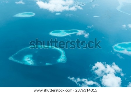 Aerial view of uninhabted tropical atoll in the middle of blue sea through the clouds