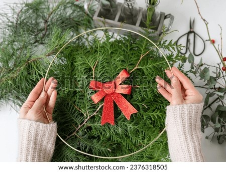 The concept of preparing for Christmas and New Year. Selective focus. A girl makes a Christmas wreath, the process of making a Christmas wreath from pine needles, thuja, shimia, rose hips, pine twigs