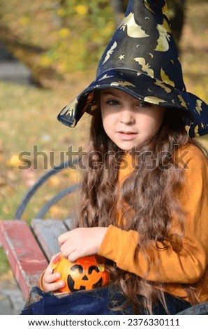 happy laughing child girl in witch costume to halloween. with a jack-o'-lantern candy bowl, trick or treat, in a witch's hat, with colorful balls in the autumn forest, eating spider-shaped candy