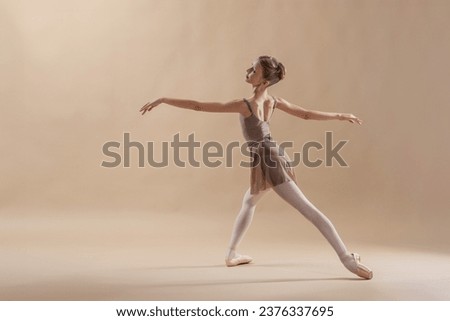 Beautiful young girl professional student ballerina in pointe shoes and a leotard on light beige background.