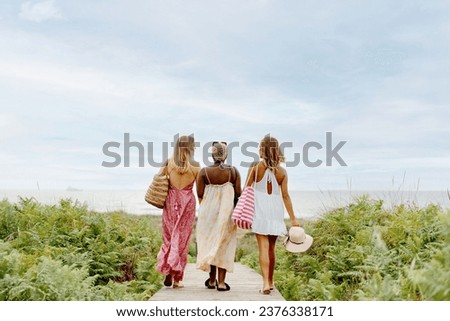Multiracial group of friends walking together towards the beach along a wooden boardwalk. girls enjoying a day at the beach. Royalty-Free Stock Photo #2376338171