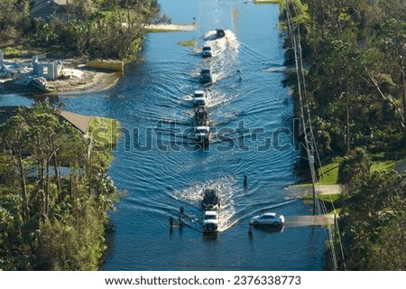 Flooded American street with moving vehicles and surrounded with water houses in Florida residential area. Consequences of hurricane natural disaster Royalty-Free Stock Photo #2376338773