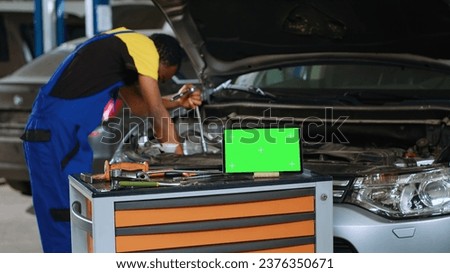 Engineer in car service uses torque wrench to secure bolts inside vehicle with green screen tablet in front. Expert utilizes professional tools to mend out of order automobile next to mockup device