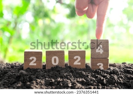 Human hand change year 2023 to 2024 in wooden blocks with growing plant at sunrise. Welcome new year 2024 and goodbye 2023 concept.