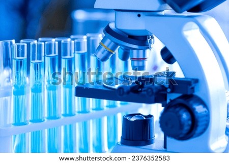 Test tubes with light blue liquid in researched laboratory.Test tubes with medical sample substance and microscope in laboratory. Royalty-Free Stock Photo #2376352583