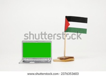 Selective focus picture of Green Chroma Key laptop with waving Palestinian flag insight. Support for Palestine on internet.
