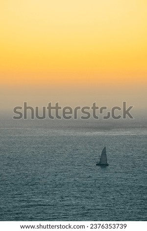a sailboat in a peaceful ocean and sunset scenery on a cloudless evening with vibrant golden light