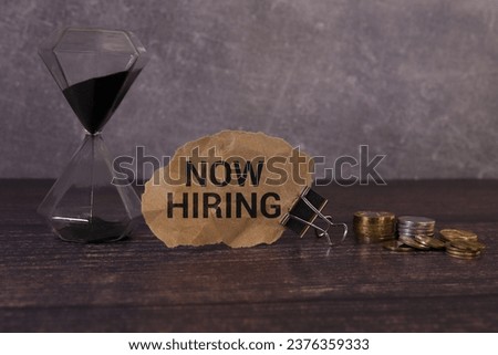 Now hiring message on card with a pushpin on a corkboard.