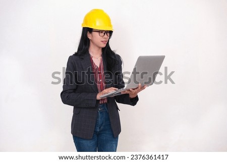 A young Asian woman wearing glasses and a safety helmet is working on a laptop Royalty-Free Stock Photo #2376361417