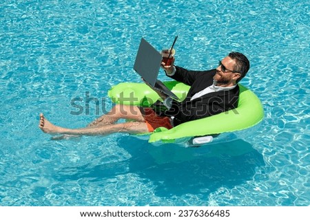 Funny freelancer, distance online work, e-working. Summer funny business. Business man in suit remote working on laptop in water pool. Business man working online on laptop in summer pool. Royalty-Free Stock Photo #2376366485