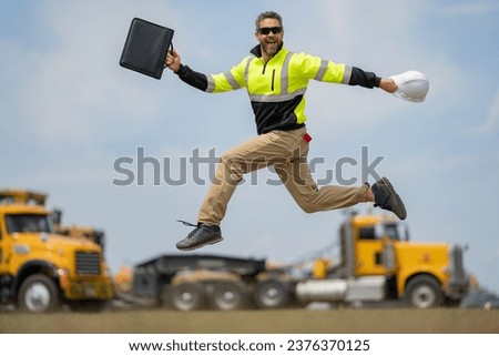 Construction man excited jump with helmet. Builder in helmet outdoor portrait. Worker in hardhat. Construction engineer worker in builder uniform on construction. Excited foreman jump. Royalty-Free Stock Photo #2376370125
